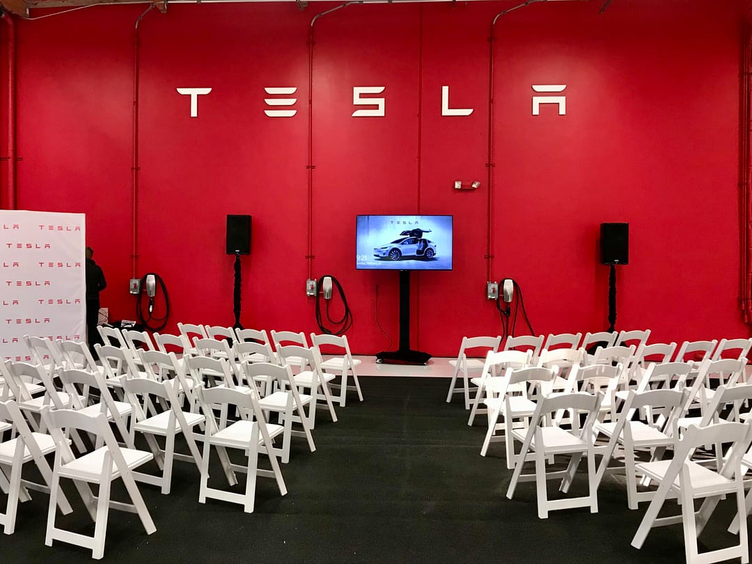 75'' monitor set up for Tesla event with two powered speakers next to it.
